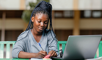 Jeune femme qui prend des notes alors qu'elle suit un cours en ligne sur son ordinateur