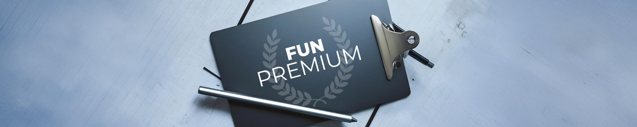 Sur un support pour écrire gris anthracite, on voit les mots "FUN PREMIUM" en blancqui se détachent. Un stylet argenté est posé sur le bord de la tablette. Le fond de l'image est gris souris.